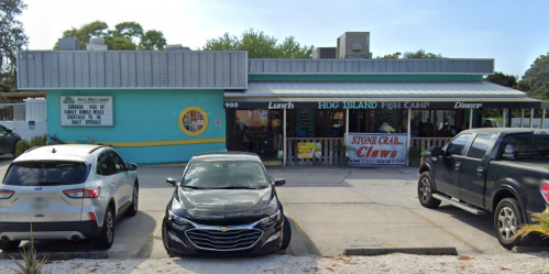 A colorful restaurant exterior with a sign reading "Hoo Island Fish Camp" and parked cars in front.