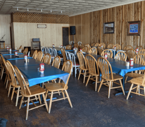 Empty dining area with wooden chairs and blue tablecloths, featuring multiple tables set for guests.