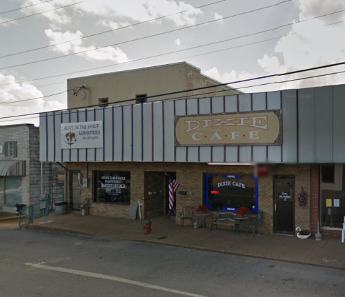 A small town building featuring the Dixie Café sign and a ministry storefront, with a cloudy sky above.