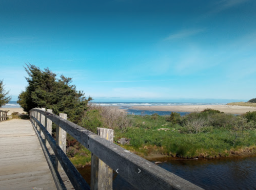 A wooden walkway leads to a scenic beach with blue skies and greenery on either side.