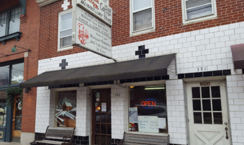 A brick building with a tiled facade, featuring a sign for a café and an open neon sign in the window.