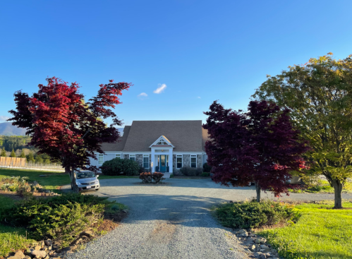 A scenic view of a house surrounded by vibrant trees and a gravel driveway under a clear blue sky.