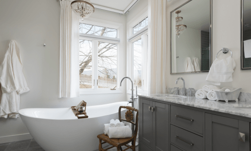 A modern bathroom featuring a freestanding tub, gray cabinetry, and large windows with natural light.