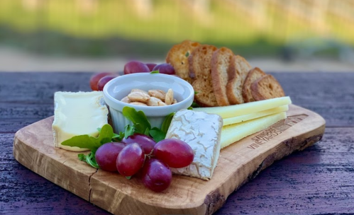 A wooden platter with cheese, grapes, nuts, and crackers, set against a blurred outdoor background.