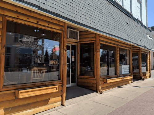 A rustic wooden restaurant exterior with large windows, featuring an "OPEN" sign and outdoor seating.