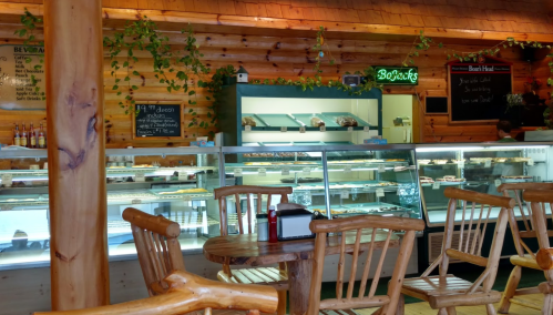 A cozy café interior with wooden decor, showcasing a display case filled with pastries and seating at rustic tables.
