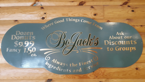 Sign for BoJack's featuring donut prices and a note about group discounts, with a decorative design on a wooden floor.