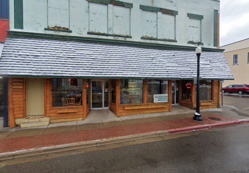A rustic storefront with a snow-covered roof, featuring large windows and wooden accents, on a rainy street.