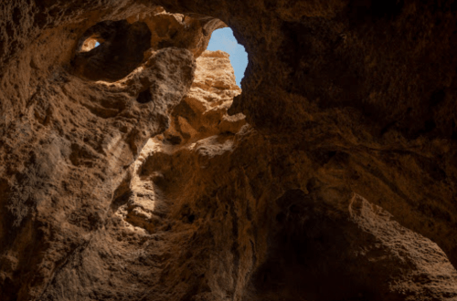 View looking up from inside a rocky cave, with sunlight streaming through an opening above.