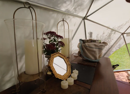 A cozy indoor setup featuring candles, a small mirror, flowers, and a basket in a geodesic dome.