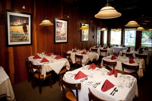 Cozy restaurant interior with wooden walls, tables set with white tablecloths, and vintage travel posters on the walls.