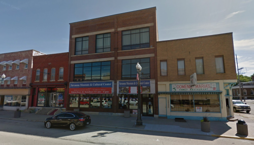 A street view of a two-story building housing the Sycamore Museum & Cultural Center, with nearby shops and a restaurant.