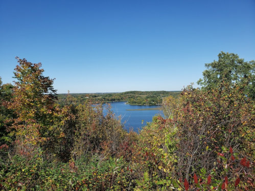 A scenic view of a lake surrounded by colorful autumn foliage under a clear blue sky.