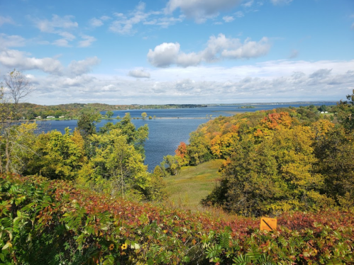 A scenic view of a lake surrounded by colorful autumn foliage and a blue sky with scattered clouds.