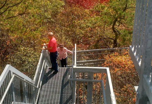 Two people walking on a metal staircase surrounded by colorful autumn foliage.