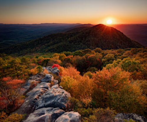 A stunning sunset over rolling hills, surrounded by vibrant autumn foliage and rocky outcrops.