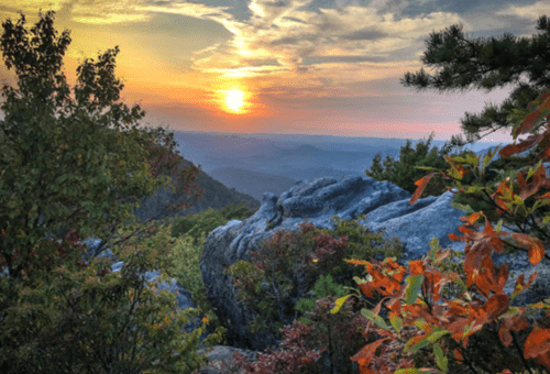 Sunset over a mountain landscape, with vibrant autumn foliage in the foreground and a colorful sky.