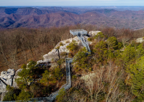 Aerial view of a rocky outcrop with a winding staircase, surrounded by trees and mountains in the background.