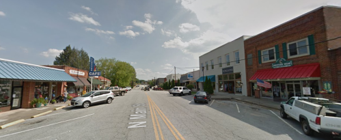 A small town street lined with shops and cafes, featuring parked cars and a clear blue sky.