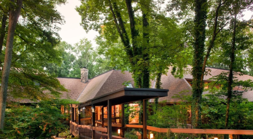 A cozy house nestled among lush green trees, featuring a wooden deck and warm lighting.