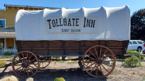 A covered wagon with "Tollgate Inn" and "Sandy Oregon" signage, displayed outdoors near a building.