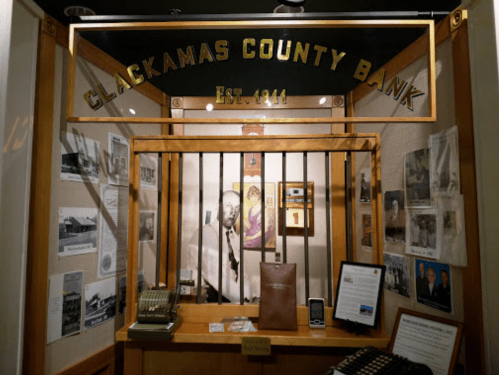 Display of Clackamas County Bank with historical photos, artifacts, and a vintage cash register. Established 1911.