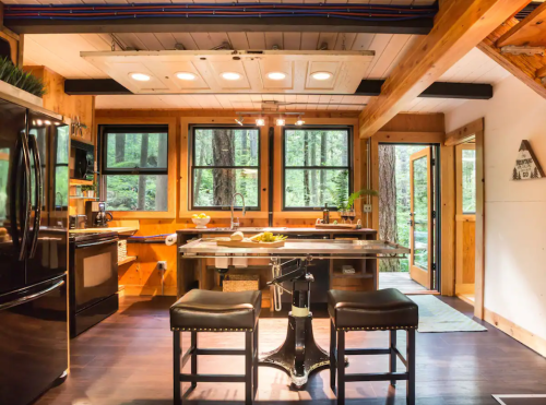 Cozy kitchen with wooden accents, modern appliances, and large windows overlooking a forested area.