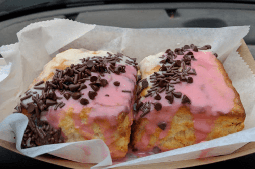 Two pastries topped with pink icing and chocolate sprinkles, served in a paper tray.