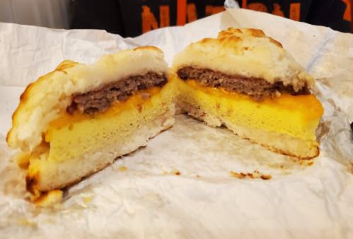 A cross-section of a sandwich featuring layers of sausage, cheese, and egg between two biscuit halves.