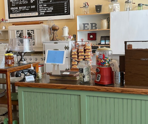 A cozy café counter with a cash register, snacks, a gumball machine, and a menu board in a warm, inviting setting.