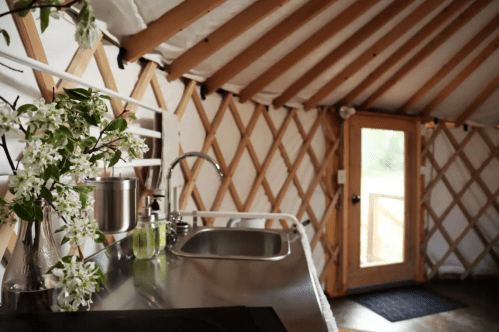 A cozy kitchen with a stainless steel sink, wooden beams, and a door leading outside, adorned with fresh flowers.