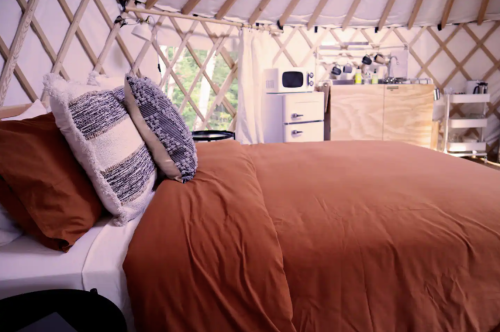 Cozy interior of a yurt featuring a bed with brown bedding and a kitchenette in the background.