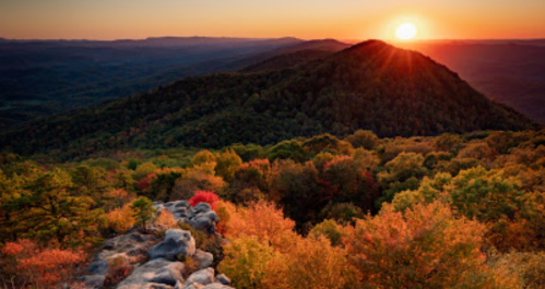 A vibrant sunset over a mountain landscape, surrounded by colorful autumn foliage and rocky foreground.