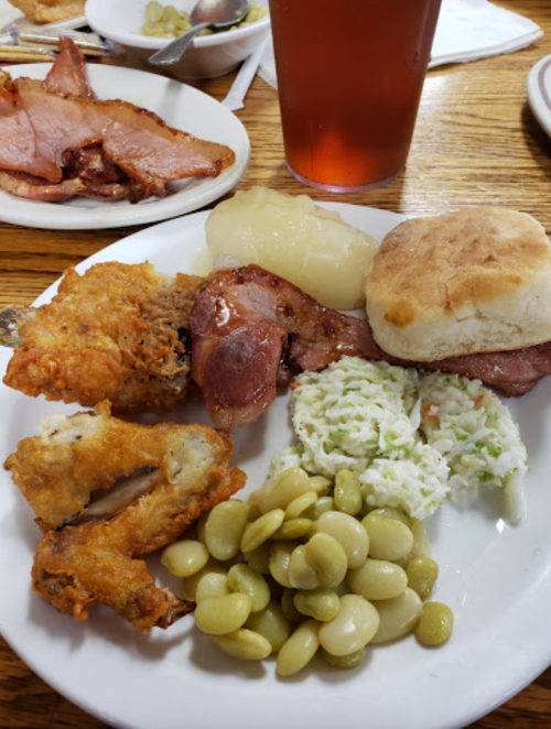 A plate of Southern comfort food featuring fried chicken, ham, biscuit, coleslaw, lima beans, and applesauce.