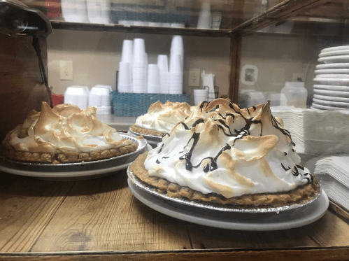 Three delicious meringue pies with golden-brown peaks displayed behind a glass case on a wooden counter.