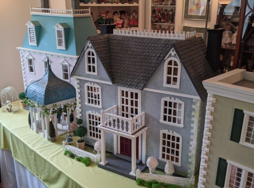 A display of three detailed dollhouses with intricate designs and landscaping on a table.