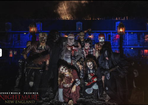 A group of costumed characters in eerie makeup poses in a dark, haunted setting with spooky lighting.
