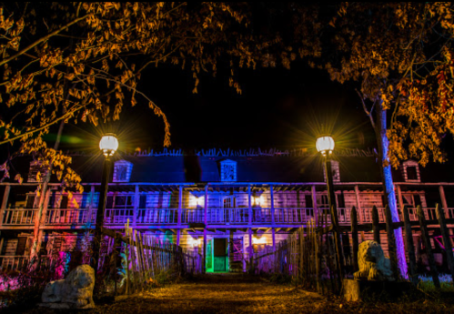 A spooky, illuminated building at night, surrounded by trees and eerie lighting, creating a haunted atmosphere.