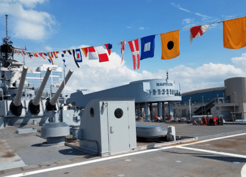 A naval ship deck adorned with colorful signal flags, featuring large cannons and a building in the background.