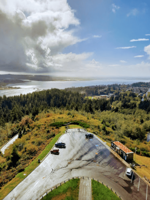 A scenic view from above, showcasing a lush landscape, a winding road, and a body of water under a partly cloudy sky.