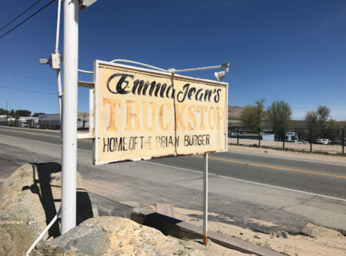 Sign for Emma Jean's Truckstop, advertising the "Brian Burger," alongside a road with a clear blue sky.