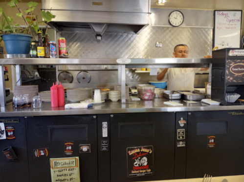 A diner kitchen with a chef preparing food behind a counter, surrounded by plates and condiments.