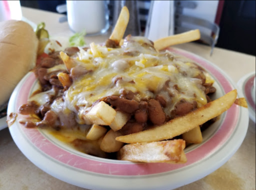 A plate of fries topped with chili, melted cheese, and beans, served alongside a hot dog and condiments.