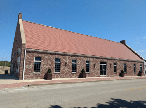 A brick building with a red roof and large windows, situated on a street under a clear blue sky.