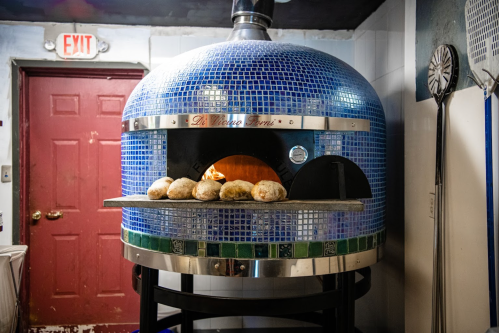 A blue-tiled pizza oven with loaves of bread baking inside, set against a red door in a cozy kitchen.