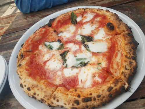A freshly baked pizza with tomato sauce, mozzarella cheese, and fresh basil on a wooden table.