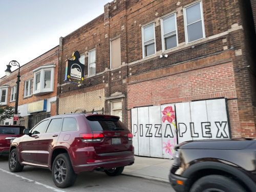 A street view of a building with a sign for "PizzaPlex" and parked cars in front.