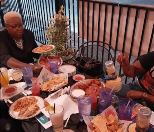 Two people enjoying a meal at an outdoor table, surrounded by plates of food and drinks.