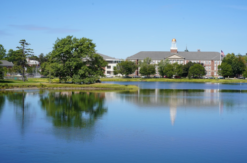A serene lake reflects a building and trees under a clear blue sky.