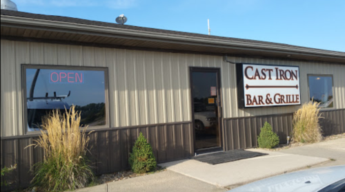 Exterior of Cast Iron Bar & Grille with an "OPEN" sign and landscaping in front. Clear blue sky above.